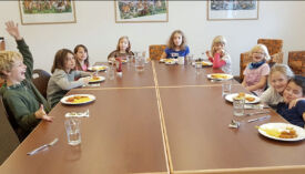 Kinder sitzen um einen grossen Tisch herum beim Mittagessen